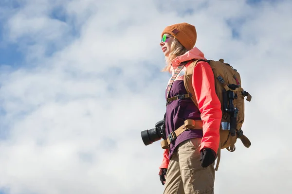 Портрет фотографа-туриста-гіпстера з фотоапаратом у сонцезахисних окулярах та капелюхом на тлі блакитного неба та хмар. Концепція подорожей фотографіями — стокове фото