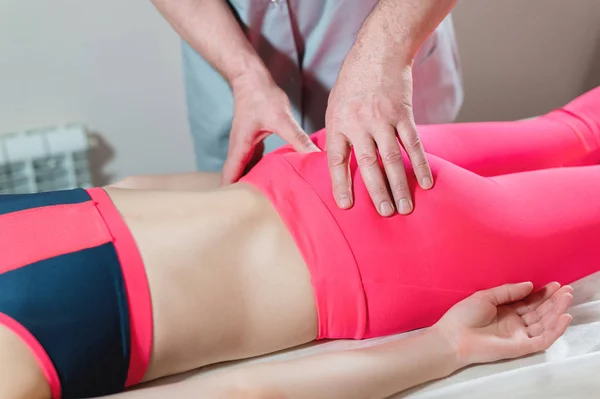 Primer plano de una edición de base de columna vertebral de chicas jóvenes por un fisioterapeuta masculino de masaje visceral. Las manos del médico establecen y amasan el coxis del paciente — Foto de Stock