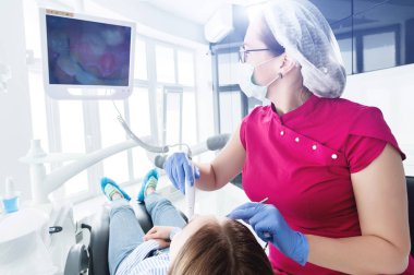 Gözlük ve tulum profesyonel bir diş hekimi kadın Led aydınlatma ile bir intraoral stamotolojik video kamera kullanarak diş sandalyesinde genç bir kızın ağız boşluğu inceler