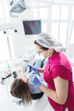 Gözlük ve tulum profesyonel bir diş hekimi kadın Led aydınlatma ile bir intraoral stamotolojik video kamera kullanarak diş sandalyesinde genç bir kızın ağız boşluğu inceler