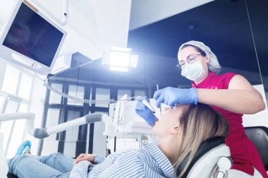 Gözlük ve tulum profesyonel bir diş hekimi kadın Led aydınlatma ile bir intraoral stamotolojik video kamera kullanarak diş sandalyesinde genç bir kızın ağız boşluğu inceler