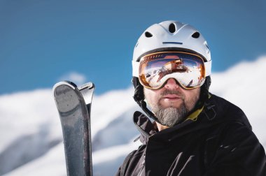 Maskeli Kafkas dağlarının yansıması olan bir kayak merkezinin karla kaplı dağlarına kask lı ve kar maskeli yakın çekim atlet kayakçı