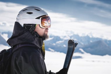 Maskeli Kafkas dağlarının yansıması olan bir kayak merkezinin karla kaplı dağlarına kask lı ve kar maskeli yakın çekim atlet kayakçı