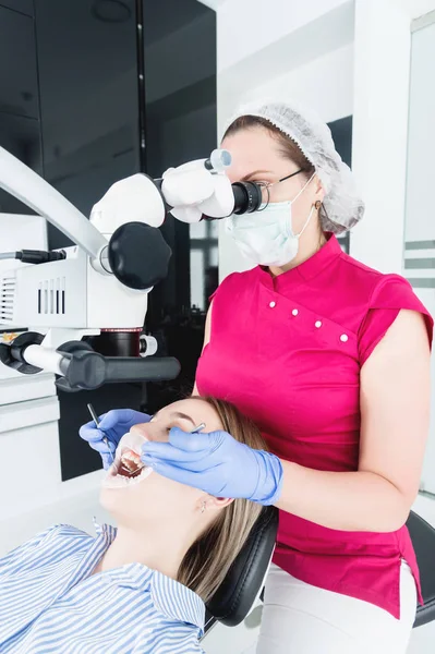 A női szakmai fogorvos vizsgálja a női beteg egy stamotologic Mikroszkóp az irodájában. Stamotologist szakmai koncepció — Stock Fotó
