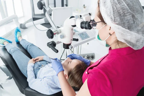 女性専門の歯科医が、彼女のオフィスで立体顕微鏡で女性患者を診察します。スタモトロジスト職業概念 — ストック写真