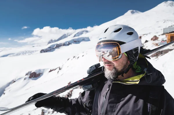 Close-up Retrato barbudo esquiador do sexo masculino envelhecido contra o fundo das montanhas. Um homem adulto usando óculos de esqui máscara e esquis capacete em seu ombro parece montanhas. Conceito de resort de esqui — Fotografia de Stock