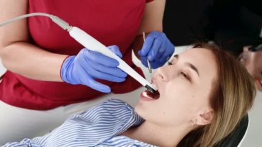 Gözlük ve tulum profesyonel bir diş hekimi kadın Led aydınlatma ile bir intraoral stamotolojik video kamera kullanarak diş sandalyesinde genç bir kızın ağız boşluğu inceler