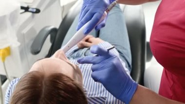 Gözlük ve tulum profesyonel bir diş hekimi kadın Led aydınlatma ile bir intraoral stamotolojik video kamera kullanarak diş sandalyesinde genç bir kızın ağız boşluğu inceler
