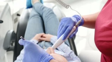 Gözlük ve tulum profesyonel bir diş hekimi kadın Led aydınlatma ile bir intraoral stamotolojik video kamera kullanarak diş sandalyesinde genç bir kızın ağız boşluğu inceler
