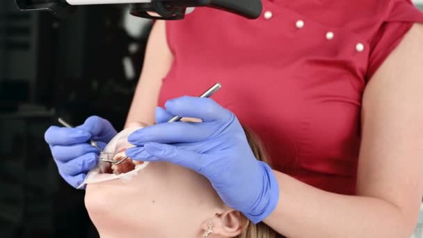 Uma dentista profissional do sexo feminino examina uma paciente com um microscópio estomatológico em seu consultório. Conceito de profissão de estamotologista — Vídeo de Stock