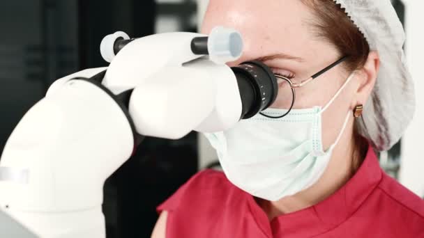 Nahaufnahme einer Frau in Brille mit einem professionellen Zahnarzt, der in ihrem Büro mit einem professionellen stamotologischen Mikroskop arbeitet. Berufskonzept für Stammzellenforscher — Stockvideo