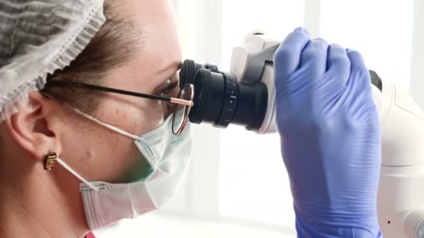 Közeli egy nő a szemüveg egy profi fogorvos dolgozik a szakmai stamotological Mikroszkóp az irodájában. Stamotologist szakmai koncepció — Stock videók