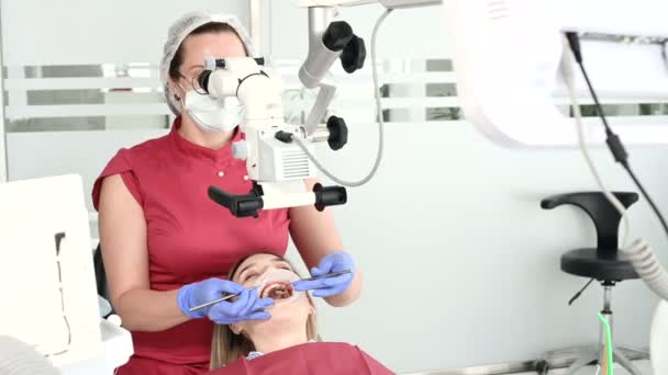 Жінка-професіонал-стоматолог вивчає пацієнта-жінку зі стоматологічним мікроскопом в її кабінеті. Концепція професії стоматолога — стокове відео