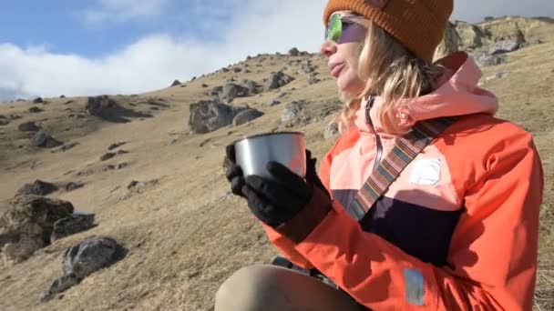 Портрет красивой девушки в шляпе и солнцезащитных очках с кружкой в руках - пить кофе или чай, сидя на камне в горах. Концепция туризма и отдыха в горах — стоковое видео