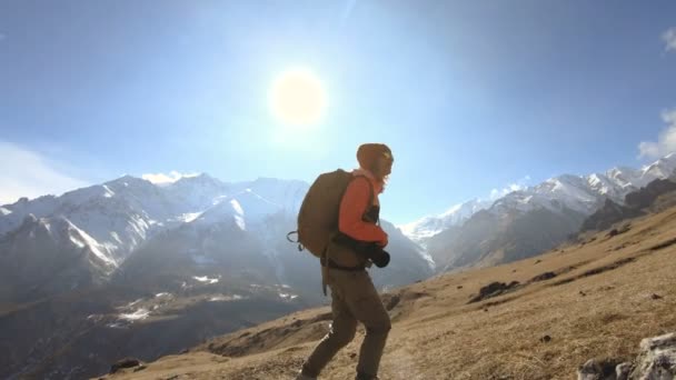 Fotógrafo de menina viajante feliz em óculos de sol com uma câmera e uma mochila sobe em um fundo de picos cobertos de neve em um dia ensolarado — Vídeo de Stock