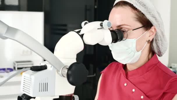 Zbliżenie Kobieta w okularach z profesjonalnym dentystą współpracując z profesjonalnym mikroskopem stamotologicznym w swoim biurze. Koncepcja zawodu stamotologa — Wideo stockowe