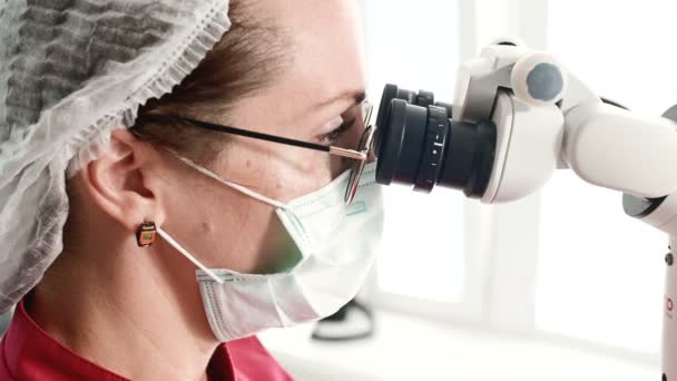特写 一位戴着眼镜的妇女，一位专业牙医在办公室用专业的显微镜工作。葡萄球菌专业概念 — 图库视频影像