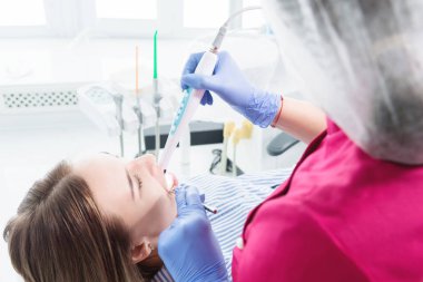 Gözlük ve tulum profesyonel bir diş hekimi kadın Led aydınlatma ile bir intraoral stamotolojik video kamera kullanarak diş sandalyesinde genç bir kızın ağız boşluğu inceler