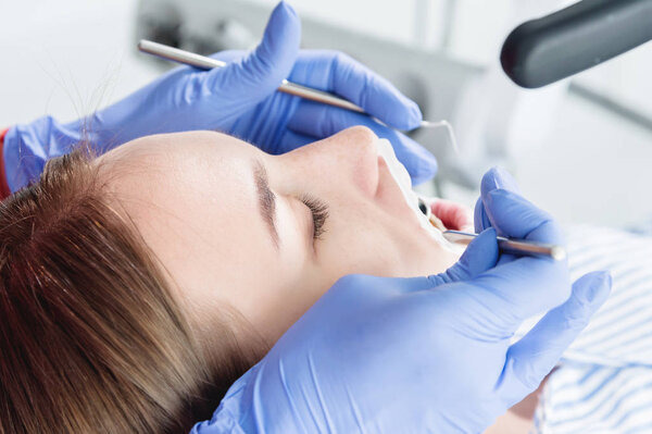 A close-up of the girls face is examined by a dental examiner with his mouth open and a napkin and eyes closed. Dentist hands with inspection tools