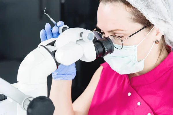 Közeli egy nő a szemüveg egy profi fogorvos dolgozik a szakmai stamotological Mikroszkóp az irodájában. Stamotologist szakmai koncepció — Stock Fotó