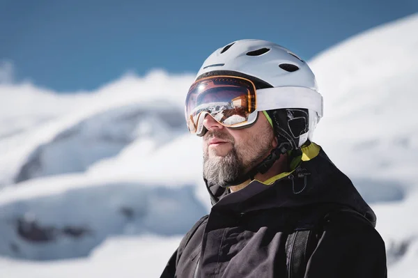 Atleta di primo piano in casco e maschera da sci contro le montagne innevate di una stazione sciistica con un riflesso delle montagne caucasiche in maschera — Foto Stock