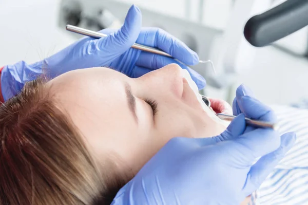 Um close-up do rosto das meninas é examinado por um examinador dentário com a boca aberta e um guardanapo e olhos fechados. Mãos de dentista com ferramentas de inspeção — Fotografia de Stock