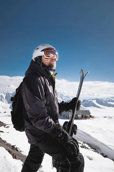 Retrato atleta esquiador em capacete e máscara de esqui contra as montanhas cobertas de neve de uma estância de esqui com um reflexo das montanhas caucasianas na máscara — Fotografia de Stock