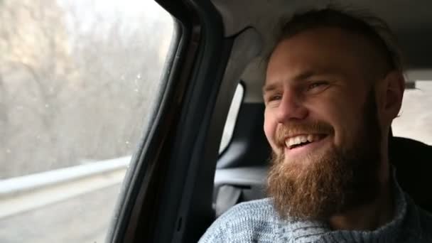 Крупный план портрета смеющегося бородатого хипстера-мужчины, сидящего в машине на заднем сидении и медитирующего, оглядываясь вокруг — стоковое видео