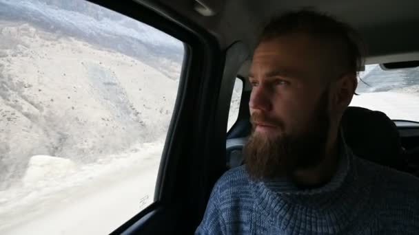 Nahaufnahme eines sprechenden bärtigen Hipstermännchens, das im Auto auf dem Rücksitz sitzt und vor dem Hintergrund der Berge seitlich meditiert — Stockvideo