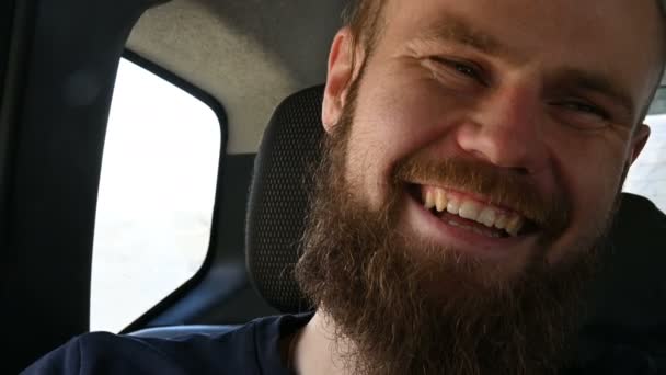 Nahaufnahme eines lächelnden bärtigen Hipster-Männchens, das auf dem Rücksitz in einem Auto sitzt und meditiert, während er sich umschaut — Stockvideo