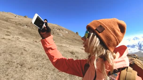 Portret van een gelukkige meisje reiziger fotograaf in een hoed en zonnebril met een camera rond zijn nek en een telefoon in zijn handen op de achtergrond van bergen neemt Foto's op zijn smartphone — Stockvideo