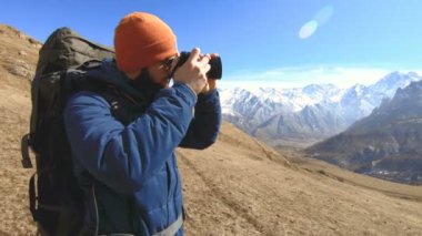 Güneş gözlüğü ve elinde bir refleks kamera ile bir şapka mutlu sakallı gezgin fotoğrafçı portresi ve dağların arka plan karşı fotoğraf çekmek. Fotoğraf seyahat konsepti
