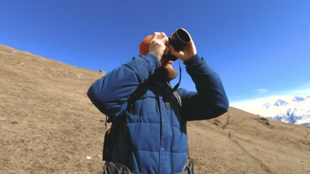 Retrato de un feliz fotógrafo barbudo viajero en gafas de sol y un sombrero con una cámara réflex en sus manos y tomando fotos sobre el fondo de las montañas. Foto concepto de viaje — Vídeo de stock