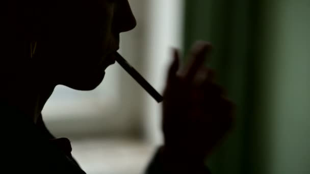 Close-up da silhueta de uma mulher rosto enfiando um cigarro em seus lábios e inflamando-a com um isqueiro e exalando fumaça. O conceito sombrio do dano de fumar em uma chave baixa — Vídeo de Stock