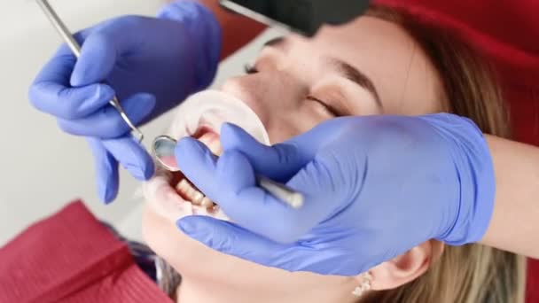 여자 얼굴의 클로즈업은 그의 입을 열고 냅킨과 눈을 감고 치과 검사관에 의해 검사됩니다. 검사 도구를 갖춘 치과 의사의 손 — 비디오