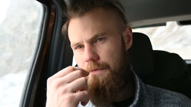 Close-up portrait of a smiling bearded hipster male with a toothpick in his mouth sitting in the car in the backseat and reflecting on the sides — Stock Video