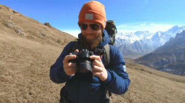 Güneş gözlüğü ve elinde bir refleks kamera ile bir şapka mutlu sakallı gezgin fotoğrafçı portresi ve dağların arka plan karşı fotoğraf çekmek. Fotoğraf seyahat konsepti