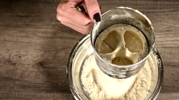 Close-up of a female hand sifting flour with a sieve mug in a metal bowl in the home kitchen. Cooking Home Baking — Stock Video