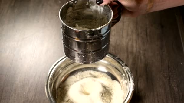 가정용 주방의 금속 그릇에 체 머그잔으로 밀가루를 체질하는 여성의 손을 클로즈업. 홈 베이킹 요리 — 비디오