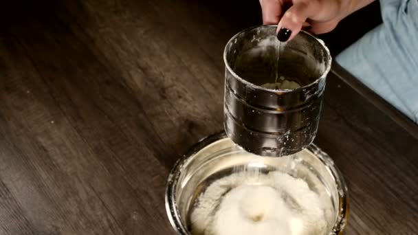 Close-up de uma mão feminina peneirando farinha com uma caneca peneira em uma tigela de metal na cozinha da casa. Cozinhar em casa Cozimento — Vídeo de Stock