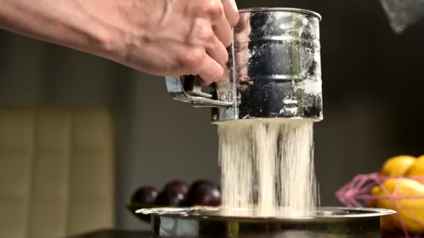 Nahaufnahme einer weiblichen Hand, die in der heimischen Küche Mehl mit einem Siebbecher in einer Metallschüssel durchsiebt. Kochen selbst gebacken — Stockvideo