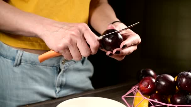 Închiderea mâinilor de sex feminin într-o bucătărie de acasă taie fructe de pădure proaspete cu un cuțit de prune și scoate un os din ele lângă un coș de lămâi. Conceptul de alimente sănătoase și vitamine — Videoclip de stoc