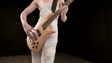 Siyah bir arka plan üzerinde bej bas gitar ile beyaz giysiler içinde genç erkek müzisyen. Bas gitarist anlamlı müzik oyunu