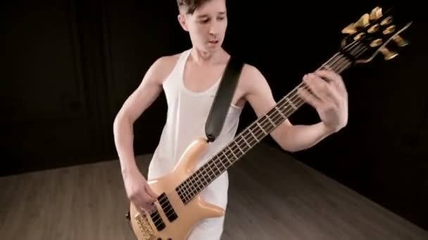 Fiatal férfi zenész, fehér ruhában, bézs basszusgitár fekete alapon. Basszusgitár játékos expresszív zenei játék — Stock videók