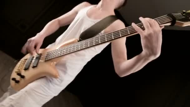 검은 배경에 베이지 색베이스 기타와 흰색 옷을 입은 젊은 남성 음악가. 베이스 기타 플레이어 표현 음악 게임 — 비디오