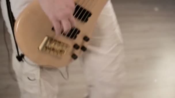Jovem músico masculino em roupas brancas com um baixo bege em um fundo preto. Baixo guitarrista expressivo jogo de música — Vídeo de Stock