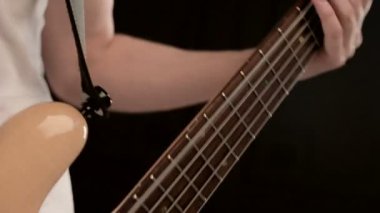 Siyah bir arka plan üzerinde bej bas gitar ile beyaz giysiler içinde genç erkek müzisyen. Bas gitarist anlamlı müzik oyunu