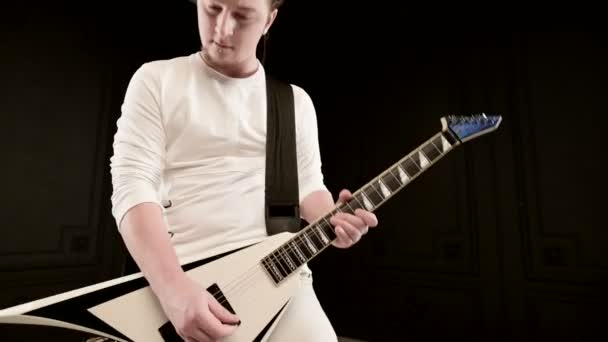 Stylischer Sologitarrist mit Dreadlocks auf dem Kopf und in weißen Kleidern auf schwarzem Hintergrund, der ausdrucksstark die weiße Gitarre in einem schwarzen Studio spielt — Stockvideo