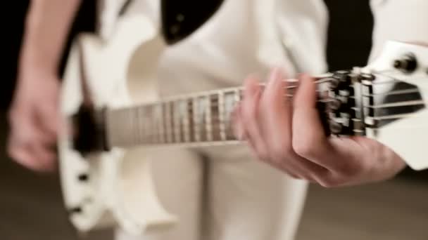 Close-up Guitarrista de ritmo elegante com diferentes olhos em roupas brancas em um fundo preto tocando expressivamente a guitarra branca em um estúdio preto — Vídeo de Stock