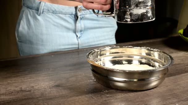 가정용 주방의 금속 그릇에 체 머그잔으로 밀가루를 체질하는 여성의 손을 클로즈업. 홈 베이킹 요리 — 비디오